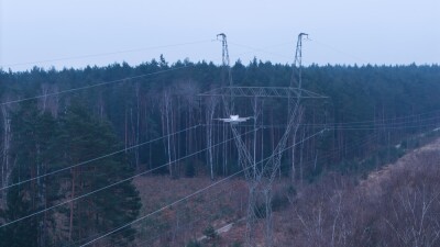 A drone flying past a high-voltage electricity pylon, capturing an aerial view of power transmission infrastructure